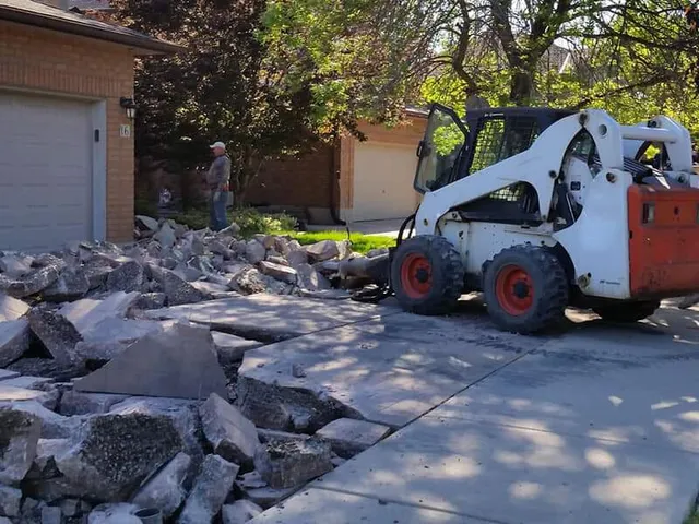 Skid steer removing broken concrete driveway